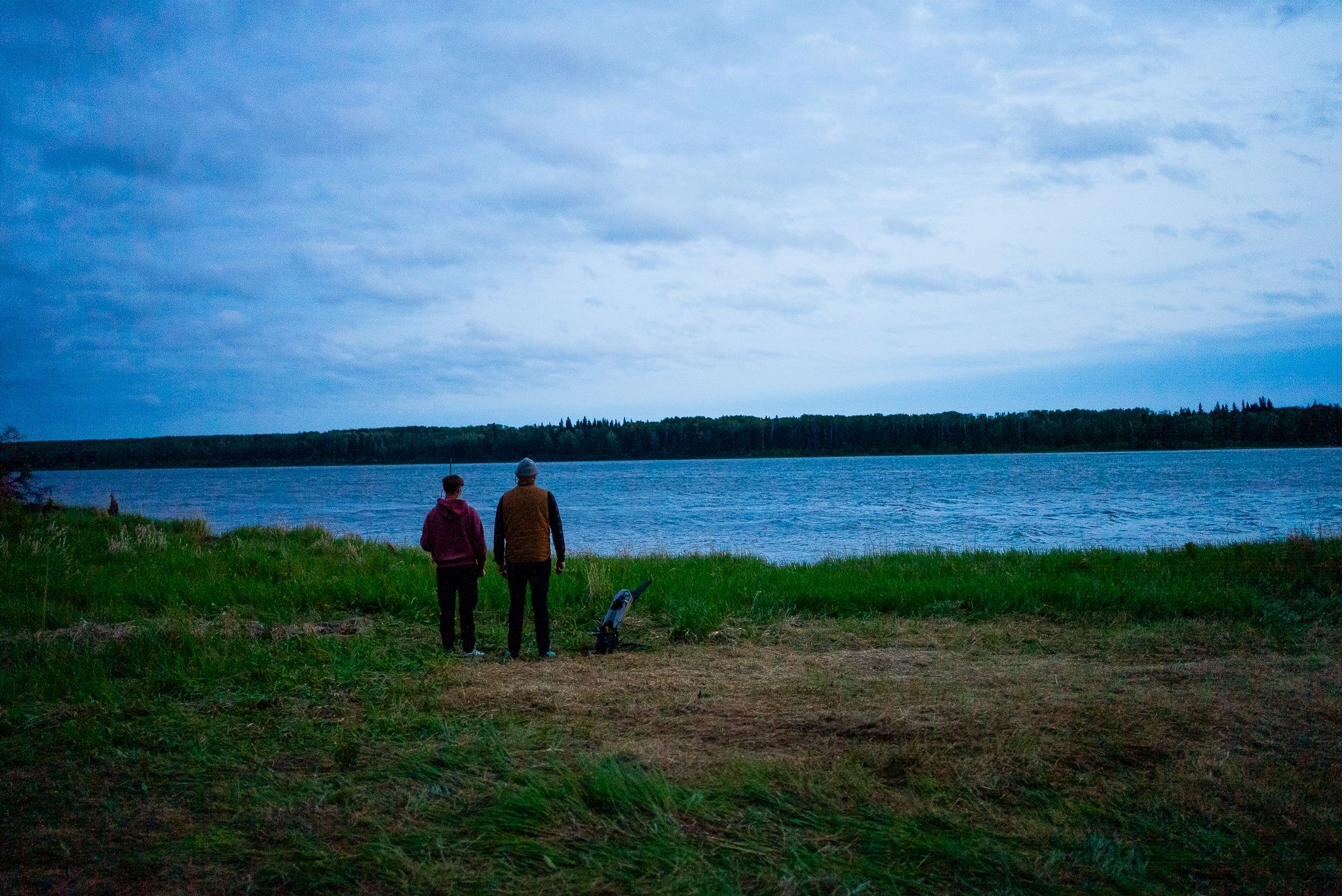 Two figures at the lake's edge in deep blue evening light