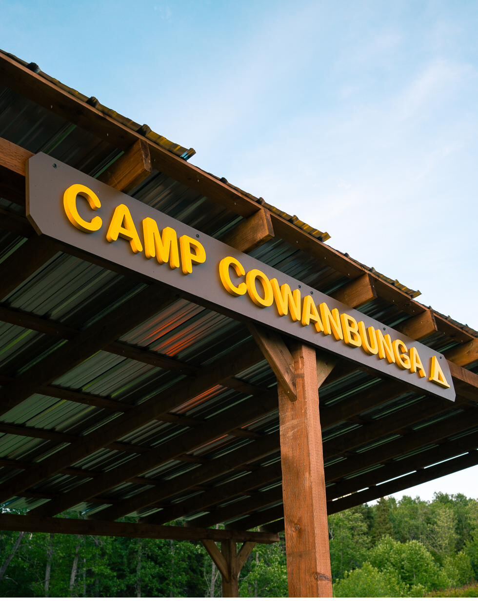 The routed wooden Camp Cowanbunga sign mounted above the pole-barn gazebo